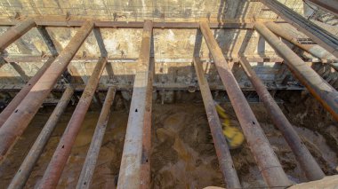 Excavators inside huge ditch pit at the construction site of the underground metro station line timelapse. Reinforcing structures from thick iron pipes of beams and structures.