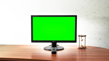 Computer green screen monitor is standing on a desk in an office timelapse hyperlapse forward motion. Design of workplace with hourglass and remote control