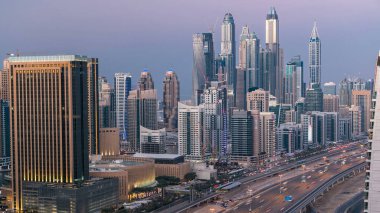Dubai Marina ve Dubai, BAE 'deki JLT gökdelenlerinin hava üzerinden gece gündüz geçiş zamanı. Modern kuleler ve Şeyh zayed yolundaki trafik metro hattı ve tramvay istasyonu yukarıdan.