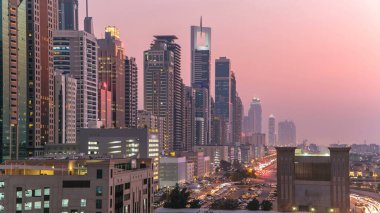 Dubai Kuleleri 'nin şehir merkezinden gece gündüz geçiş zamanı. Gün batımından sonra Şeyh Zayed 'in gökdelenli hava manzarası. Yolda ve otoparkta trafik vardı.