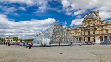 Camdan piramit ve Louvre Müzesi 'nin ana avlusu. Turistler yaz günü mavi bulutlu gökyüzüyle dolaşıyorlar. Paris, Fransa