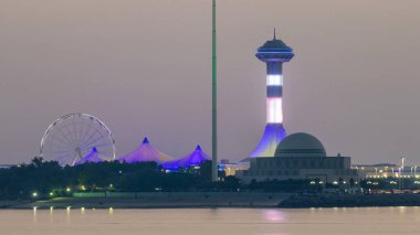 Abu Dabi 'de akşam, Marina Adası' ndan gece gündüz geçiş süresince Corniche 'in manzarası. Aydınlatılmış binalar ve su üzerindeki yansıma