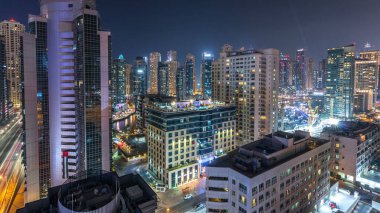 Gece görüş noktasından Dubai Marina 'nın hava görüntüsü. Parlayan pencerelerle aydınlatılmış modern gökdelenler ve konut kuleleri. Yoğun bir yolda trafik var.