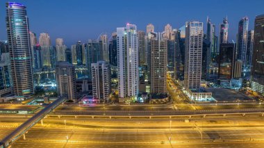 Dubai Marina gökdelenleri, güneş doğarken Dubai 'de JLT' den gündüz saatlerine kadar gökdelenler. Aydınlatılmış uzun gölgeli modern kuleler aşağı doğru ilerliyor ve Şeyh zayed yolunda trafik var..