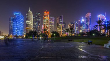 Doha 'nın yüksek katlı mahallesinde gece vakti hızlandırılmış hipervane, parktan görülmüş. Batı körfezinde aydınlatılmış gökdelenler ve palmiyeler