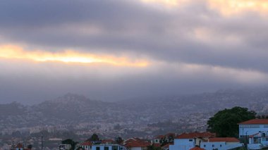 Tepedeki evlerin üzerinde bulutlarla gün batımı, Funchal, Madeira, Portekiz zaman çizelgesi