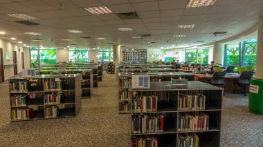 Üniversite kütüphanesindeki bilgisayar istasyonu, ön planda oturma alanı olan hiperhızlandırılmış zaman dilimi. Kutular ve raflarda bir sürü kitap var.