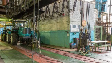 Konveyör montajı, traktörün gövdesini büyük endüstriyel fabrika zaman diliminde sahneleyecek. Traktörler montaj hattında ilerlerken tekerlekleri ve süspansiyonları kontrol et