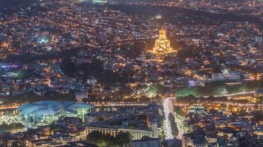 Aydınlanmış Tsminda Sameba Katedrali ya da Tiflis 'in Kutsal Üçlü Katedrali ve Kamu Hizmetleri Salonu hava gününden gece geçiş zamanına. Tiflis, Gürcistan 'daki ana katedral. Arka plandaki evler