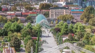 Barış Köprüsü 'nün zamanı, Kura Nehri üzerinde yay şeklinde bir çelik ve camdan köprü, Tiflis, Georgia' daki Rike Park 'tan Eski Şehir' e yürüyen insanlar.