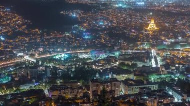 Aydınlanmış Tsminda Sameba Katedrali ya da Tiflis 'in Kutsal Üçlü Katedrali ve Kamu Hizmeti Salonu' nun gece zaman çizelgesi. Tiflis, Gürcistan 'daki ana katedral. Arka plandaki evler