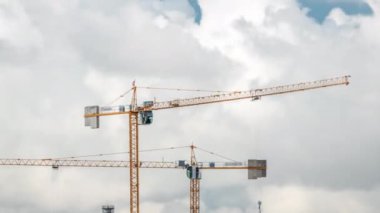 Bulutlu bir zaman dilimi olan bir bina kompleksi üzerinde çalışan ve hareket eden birkaç vinç de dahil olmak üzere büyük bir inşaat alanı. Büyük bulutlar geçip gidiyor.