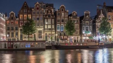 Gece vakti, Amstel Nehri 'nin kıyısındaki ünlü dans evlerinin panoramik zaman çizelgesi. Tekneli su kanalları. Hollanda, Amsterdam 'da ikonik simge ve seyahat noktası