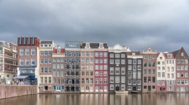 Damrak 'taki renkli Kanal Evleri' nin gece ışığında aşırı hızlanması dramatik bulutların altında geçen teknelerle suya yansıdı. Hollanda, Amsterdam 'ın büyüleyici manzarası