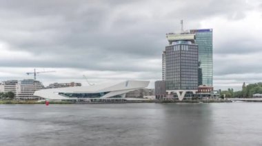 Amsterdam ufuk çizgisinin panoramik manzarasında Adam Gözcü Kulesi ve Göz Filmleri Müzesi yer alıyor. Modern binalar dramatik yağmur bulutlarının altındaki suyu yansıtır. Amsterdam, Hollanda