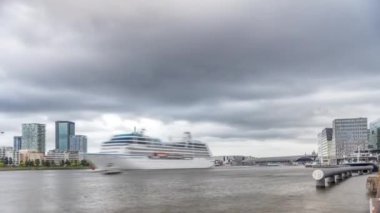 Skyline 'da Adam Gözcü Kulesi ve Göz Filmleri Müzesi yer alıyor. Modern binalar dramatik yağmur bulutlarının altındaki suyu yansıtır. Merkez istasyonun yanından geçen bir gemi var. Amsterdam, Hollanda