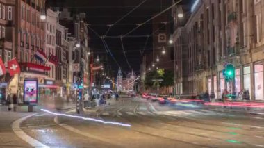 Damrak Caddesi 'ndeki elektrik tramvayı gece vakti Dam Meydanı' ndan Centraal İstasyonu 'na gidiyor. İnsanlar tramvay durağında beklerken trafik yolda ilerliyor. Amsterdam, Hollanda