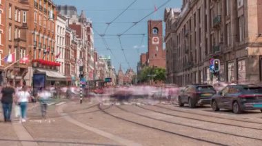 Damrak Caddesi 'ndeki elektrik tramvayı Dam Meydanı' ndan Centraal İstasyonu 'na bir zaman diliminde gidiyor. İnsanlar tramvay durağında beklerken trafik yolda ilerliyor. Amsterdam, Hollanda