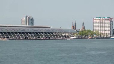 Amsterdam Merkez İstasyonu 'nun kıvrımlı çatısı ve Amstel Nehri zaman dilimi ile yakın görüntüsü. Bir feribot, bulutların hareketli olduğu güneşli bir gökyüzünün altında nehri geçer. Amsterdam, Hollanda