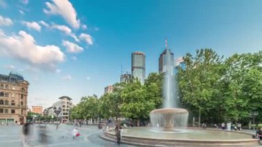 Frankfurt, Almanya 'da Opera Meydanı Operası zaman atlaması. Arka planda ağaçlarla çevrili gökdelenler ve gökyüzü altında şehir hayatı olan bir çeşme sergileniyor.