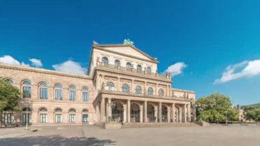 Hanover Devlet Operası Staatsoper Hannover ön görüntüsü. Şehir meydanında canlı mavi bulutlu bir zaman dilimi altında yürüyen insanların olduğu klasik tarzda bir tiyatro. Almanya