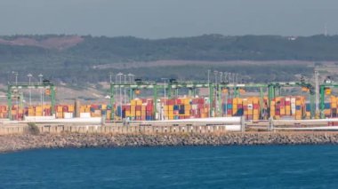Portekiz, Sines 'deki ticari liman zaman dilimi, iş lojistiği ve ulaşım endüstrisinin konteynır kargo terminalinin hava görüntüsü. Tekneler geçiyor. Çalışan vinçler ve rüzgar santralleri