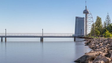 Portekiz, Lizbon 'daki Parque das Nacoes zaman diliminde Vasco da Gama Köprüsü' nün yanındaki gelgitten yükseğe hareket. Suyun seviyesi yükseliyor. Milletler Parkı 'ndaki limanda gökdelen var.