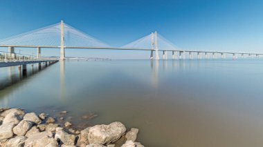 Panorama showing motion from the low to high tide next to Vasco da Gama Bridge in Parque das Nacoes timelapse in Lisbon, Portugal. Level of water is rising up. Waterfront in Park of Nations district clipart