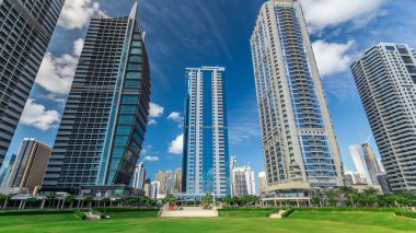 Dubai, BAE 'deki Jumeirah Gölü Kuleleri' ndeki yerleşim yerleri. Parktan yeşil çimenli mavi bulutlu gökyüzü