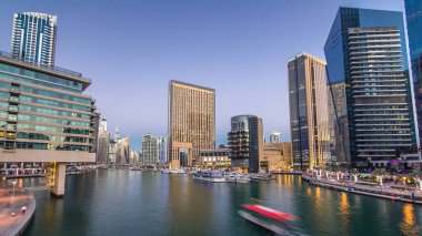 Dubai Marina rıhtımında yatları ve alışveriş merkezi yakınlarındaki modern kuleleri olan Dubai 'de güneş battıktan sonraki gece, Birleşik Arap Emirlikleri. Dubai Marina, Dubai 'de bir şehirdir.