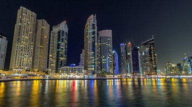 Dubai Marina gezinti güvertesinde yatlar ve modern kuleler Dubai 'deki deniz kıyısından yansıyan su, Birleşik Arap Emirlikleri' nin gece hiperhızlandırması. Yapay kanalla aydınlatılmış bölge