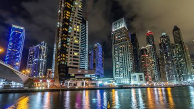 Dubai Marina güvertesi, deniz kenarındaki Birleşik Arap Emirlikleri gecesinden kalma yatlar ve modern kulelerle doludur. Çevresinde yapay kanallar ve aydınlık gökdelenler olan bir bölge.