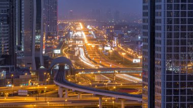 Gün geçiş timelapse ve Sheikh Zayed yolu kavşak trafik, Birleşik Arap Emirlikleri Dubai şehir manzarası gece. Işıklı modern kuleleri ve metro hattı ile gökdelenin çatı üzerinden havadan görünümü