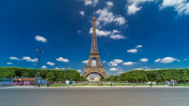Paris 'teki Champs de Mars' taki Eyfel Kulesi. Zaman atlaması, Fransa. Yazın mavi bulutlu gökyüzü, yeşil çimenler ve etrafta trafik olan çeşme.