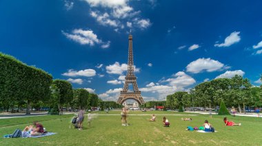 Paris 'teki Champs de Mars' taki Eyfel Kulesi. Zaman atlaması, Fransa. Yazın mavi bulutlu gökyüzü yeşil çimlerle kaplı ve insanlar etrafta dolaşıyor. İlerliyorum.