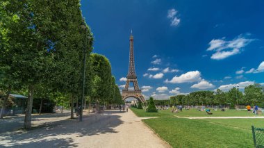 Paris 'teki Champs de Mars' taki Eyfel Kulesi. Zaman atlaması, Fransa. Yazın mavi bulutlu gökyüzü Ağaçlı yeşil çimenler ve etrafta yürüyen insanlar.