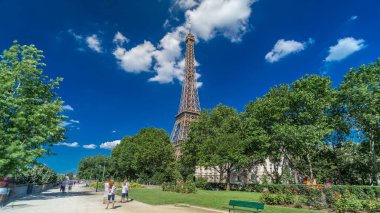 Eiffel Kulesi, Paris 'teki Siene nehri kıyılarından gösterildi. Zaman ayarlı hiperhız, Fransa. Yazın mavi bulutlu gökyüzü Yeşil ağaçlar ve etrafta yürüyen insanlar
