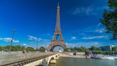 Paris 'teki Siene Nehri üzerinde köprüsü olan Eyfel Kulesi. Zaman atlaması, Fransa. Yazın mavi bulutlu gökyüzü Yeşil ağaçlar ve köprüde yürüyen insanlar