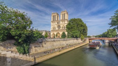 Notre Dame de Paris katedralinin ön cephesinde, nehir ve kıyı şeridi hiperhızlandırılmış. Köprüden panoramik görüntü. Yazın mavi bulutlu gökyüzü