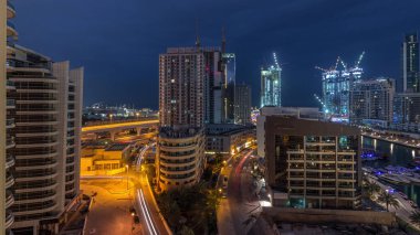 Dubai Marina 'da aydınlık gökdelenler ve gece gündüz gezinti güvertesi geçiş zamanı. Yol trafiği olan modern kuleler ve tekneler. Birleşik Arap Emirlikleri
