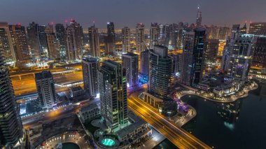 Dubai Marina gece gündüz geçiş timelapse havadan üst görünümü. Dubai, Bae gün doğumundan önce yüzen yatlar ve tekneler ile gezinti ve kanal. Işıklı modern kuleler ve yolda trafik