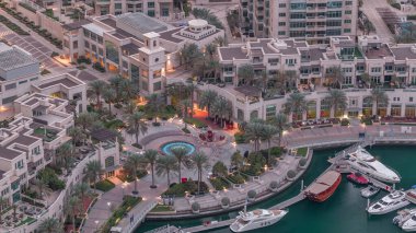 Dubai Marina Yürüyüşü 'nde çeşme ve palmiyeli Top View gece gündüz geçiş zamanı. Sabahları yat ve teknelerle aydınlatılmış.