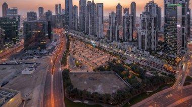Business Bay, Dubai, Uae 'de birçok gökdelenden geceye geçiş süresine sahip konut ve ofis kompleksi. Körfez Bulvarı Parkı 'nın yanındaki büyük otoparkta arabalar ve trafik vardı.