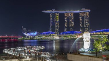 Merlion Çeşmesi, Singapur 'daki Marina Bay Sands Oteli' nin önüne su püskürtür. Köprüde insanlar var..