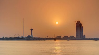Abu Dabi 'de günbatımı Marina Adası üzerinde, Corniche manzaralı. Turuncu sıcak ışık ve suyun yansıması. Vinçli inşaat alanı