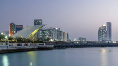 Abu Dabi 'deki gezinti alanı gün batımında aydınlandı, gece gündüz geçiş zamanı, Birleşik Arap Emirlikleri. Arka plandaki gökdelenler suya yansıdı
