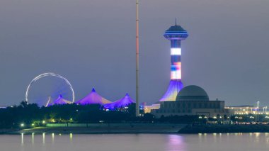 Abu Dabi 'de akşam, Marina Adası' ndan gece gündüz geçiş süresince Corniche 'in manzarası. Aydınlatılmış binalar ve su üzerindeki yansıma