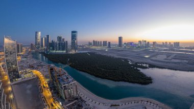 Skyscrapers on Al Reem and Al Maryah Island in Abu Dhabi day to night transition timelapse after sunset from above. Aerial panoramic cityscape from Al Reem Island with illuminated buildings clipart