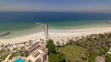 Ajman zaman diliminde, Arap Körfezi 'nin turkuaz sularının yakınında güzel bir plaj alanı. Yüzme havuzlu panoramik çatı manzarası. Deniz kıyısı ve limanı