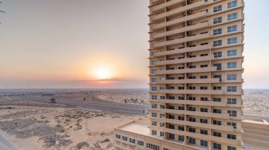 Ajman 'da gün batımı, çatıdaki zaman ayarlı hava manzarası. Birleşik Arap Emirlikleri 'ndeki bir iskan kulesinin arkasındaki turuncu bulutlu gökyüzünde akşam manzarası.